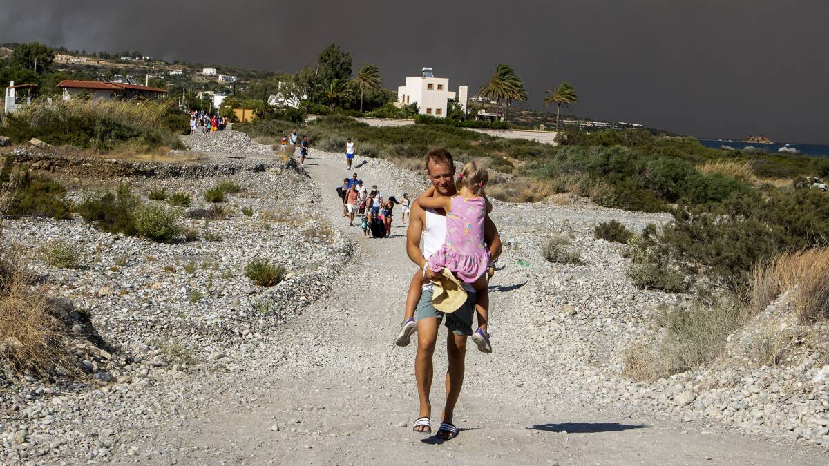 A man carries a child as they evacuate from a large wildfire on the island of Rhodes, Greece on July 22. Picture by Lefteris Diamanidis/InTime News via AP